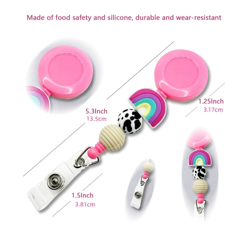 A pink retractable badge reel with a decorative beaded strap featuring a rainbow, cow print, and striped bead, shown with multiple size measurements and close-up detail views on a white background.