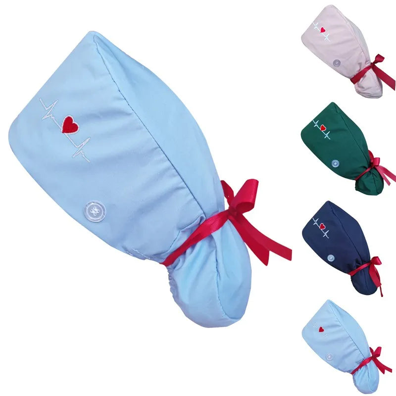 A light blue nurse cap with a red ribbon bow and embroidered heart and heartbeat design, shown on a white background with smaller color variants in pink, green, navy, and light blue.